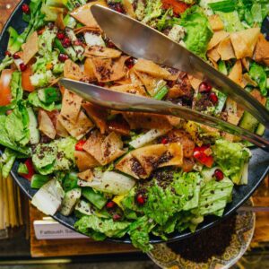 A vibrant Fattoush salad showcasing fresh vegetables, pita chips, and pomegranate seeds in a black bowl.